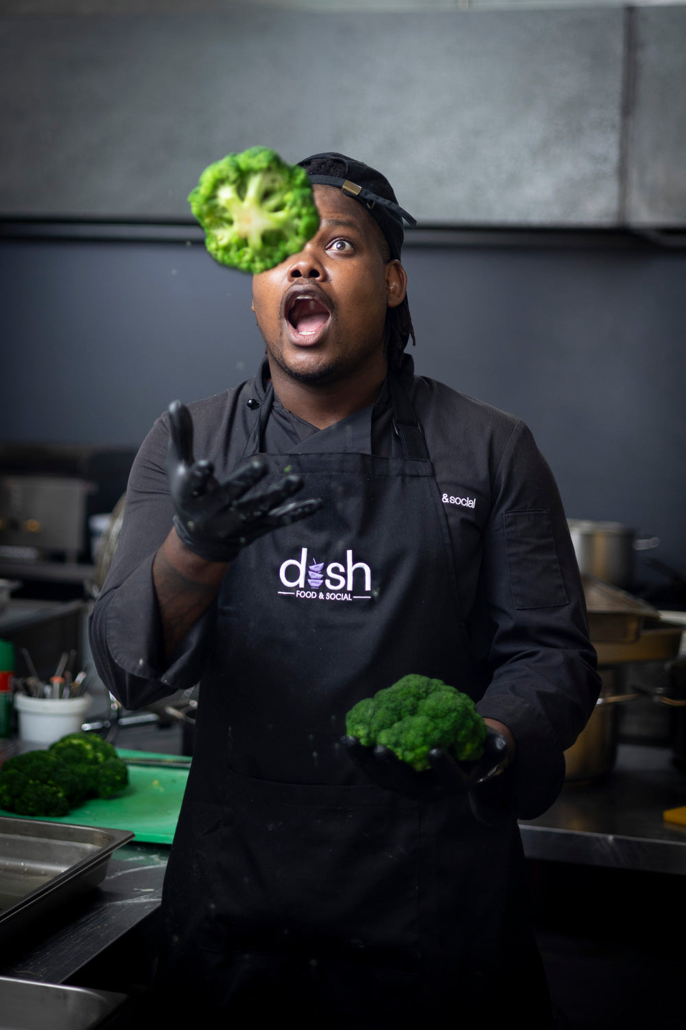 Person in a kitchen wearing a 'dish' apron, holding broccoli.