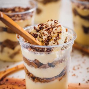 Four individual cups filled with tiramisu: layers of mascarpone and savoiardi biscuits dipped in espresso, dusted with cocoa